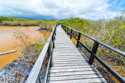 Footbridge over river against cloudy sky