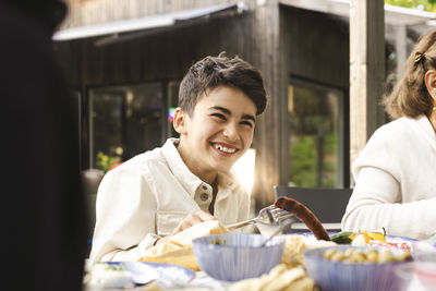 Cheerful boy sitting at dining table in patio during dinner party