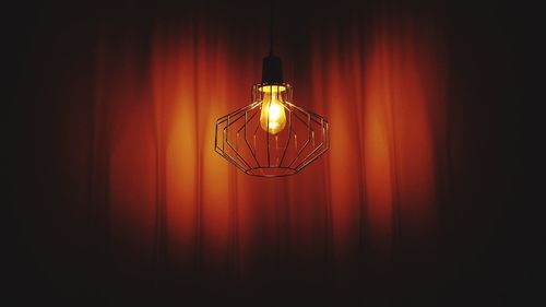 Illuminated light bulb hanging against curtain in dark theater