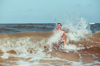 Shirtless teenage boy enjoying in sea against sky during sunny day