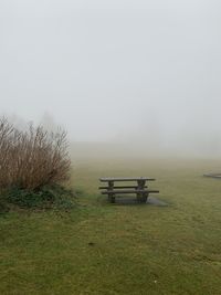 Empty bench on field against sky