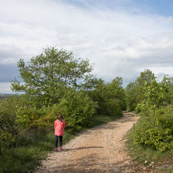 Rear view of woman walking on road amidst trees against sky