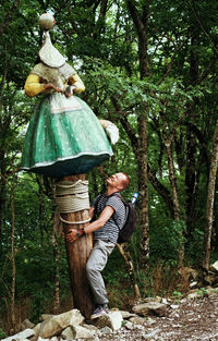 Full length of man holding female sculpture against trees at forest