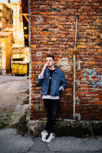 Young man smoking while standing against brick wall