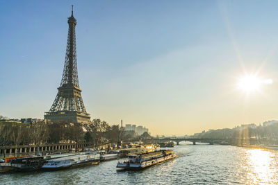 Eiffel tower by river in city against sky during sunset