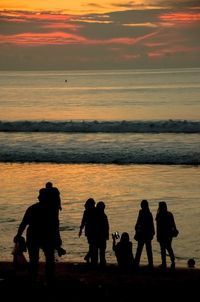 Silhouette people on beach against sky during sunset