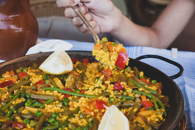 Vegan paella with rice and some vegetables. hand grabs a spoon with a portion.