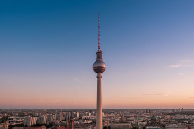 Communications tower in city against sky during sunset