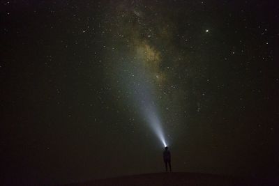 Silhouette of man holding flashlight while standing on land against sky at night