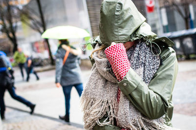 Woman pulling hood of raincoat while standing on street