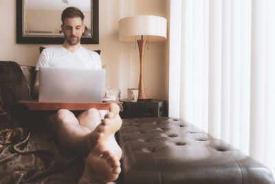 Midsection of man using mobile phone while sitting on bed