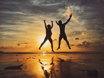 Silhouette couple jumping at beach during sunset