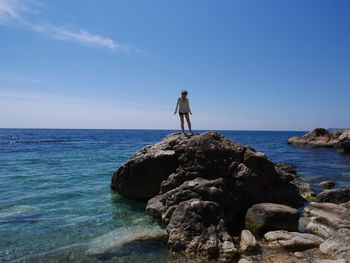 Full length of woman standing on rock at sea shore against sky