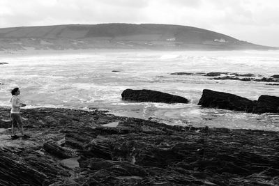 Full length of woman standing on rock by sea at baggy point