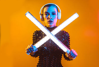 Woman in dress dancing with illuminated lights against orange background