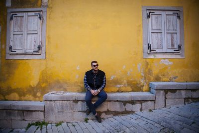 Portrait of young man sitting on window of house