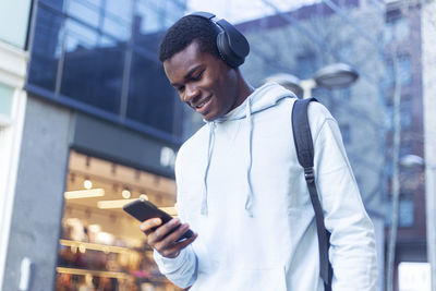 Young man with headphones using mobile phone in city