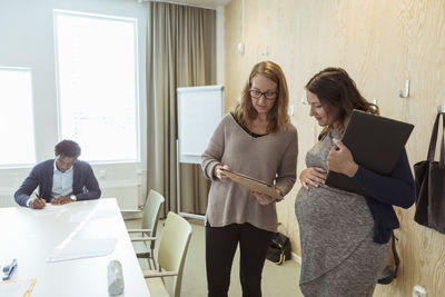 Businesswoman showing document to pregnant woman while businessman working in background at conference table