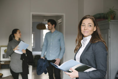 Confident female realtor holding brochure while couple standing in background