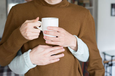 Cropped hands of man embracing boyfriend holding cup