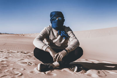 Low section of man standing on sand against clear sky