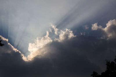 Low angle view of sunlight streaming through clouds