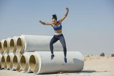 Woman jumping over pipe against sky