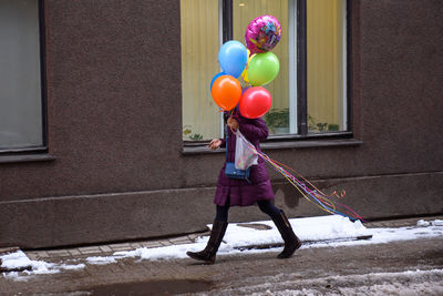 Rear view of woman with balloons standing at street during winter