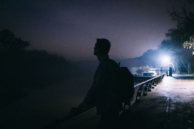 Silhouette man standing by illuminated tree against sky at night