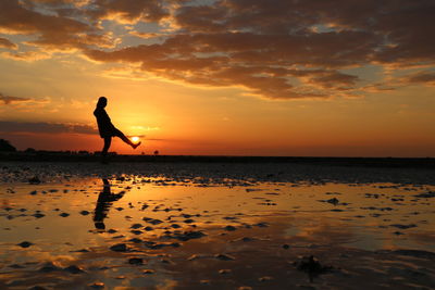 Optical illusion of woman kicking sun while standing at beach during sunset