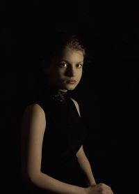 Portrait of young woman standing against black background