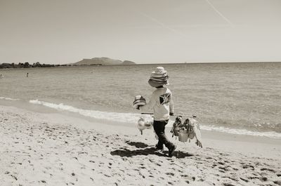 Rear view full length of vendor with hats walking on shore at beach