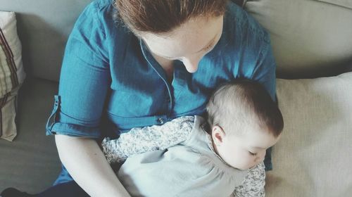 High angle view of mother carrying sleeping baby girl while sitting on bed at home