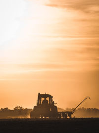 Silhouette cranes on field against sky during sunset