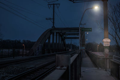 Lighting equipment by railroad tracks against sky at dusk