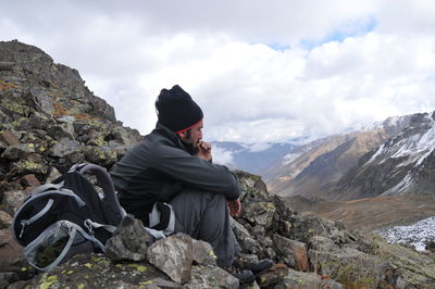 Side view of hiker sitting on mountain against cloudy sky