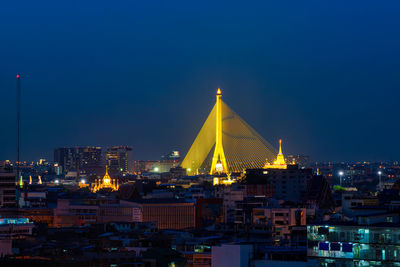 Illuminated buildings against blue sky at night