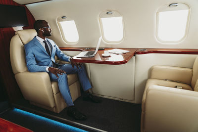 Businessman looking through window with laptop on table in airplane