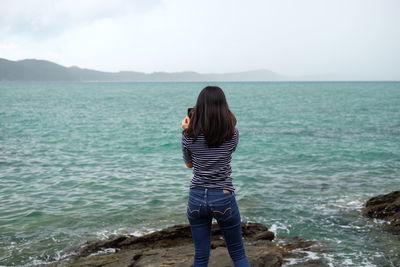 Rear view of woman standing at beach against sky