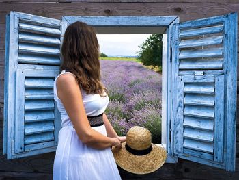 Woman in white dress looking out the open window at a field of lavender flowers