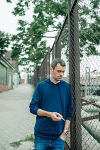 Young man looking away while standing on chainlink fence