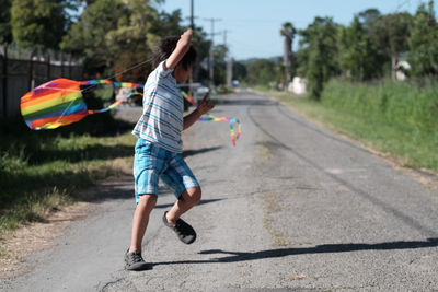 Full length of boy playing with kite on road against sky