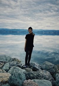 Young man standing on rock by sea against sky