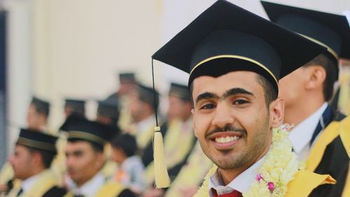 Portrait of smiling young man wearing graduation gown standing with students