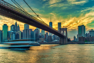 Bridge over river with buildings in background at sunset