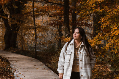 Portrait of young adult woman walking on wooden path in forest in autumn.