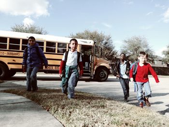 Boys walking on street by school bus against sky