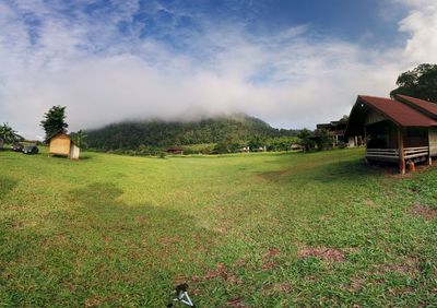 Scenic view of field by houses against sky