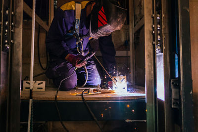 A caucasian man welding metal inside an elevator under construction