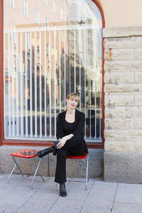 Full length portrait of confident businesswoman sitting on chair outside office